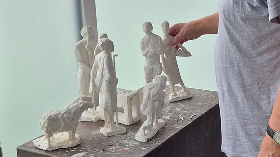 Ein Krippe zum Anfassen Ein Mann fasst eine Krippenfigur aus Gips an. Sie steht mit anderen Figuren auf einem Podest.
